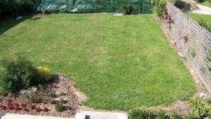 A well-maintained grassy yard with a stone wall and a small garden bed. - Apartment with large garden prox. from the sea and landing beaches (Étréham)