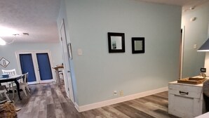 Un vaste espace de vie doté d’un parquet en bois disposé en point de Hongrie, de murs bleu clair et d’un coin repas avec une table et des chaises.