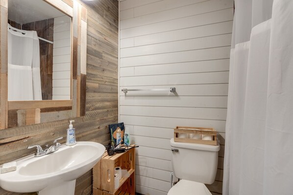 Et badeværelse med trævæg, hvid vask, toilet og bruseforhæng.