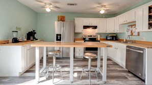 Une cuisine moderne avec des meubles blancs, un plan de travail en bois, un réfrigérateur, un lave-vaisselle et deux tabourets de bar.