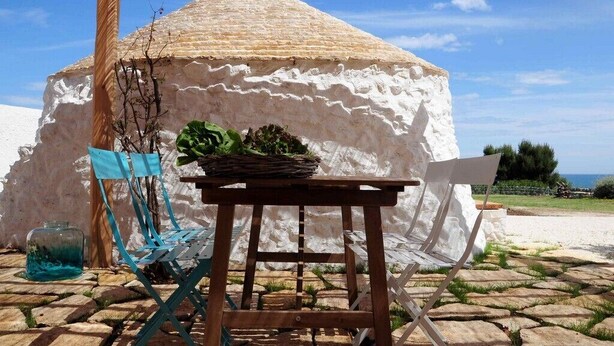A rustic outdoor seating area with a table and chairs, a woven basket, and a glass jar.