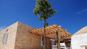 A stone building with a wooden pergola and a tree in front.
