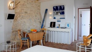 A rustic room with a stone wall, a wooden table with chairs, a white radiator, and a shelf with blue bottles.