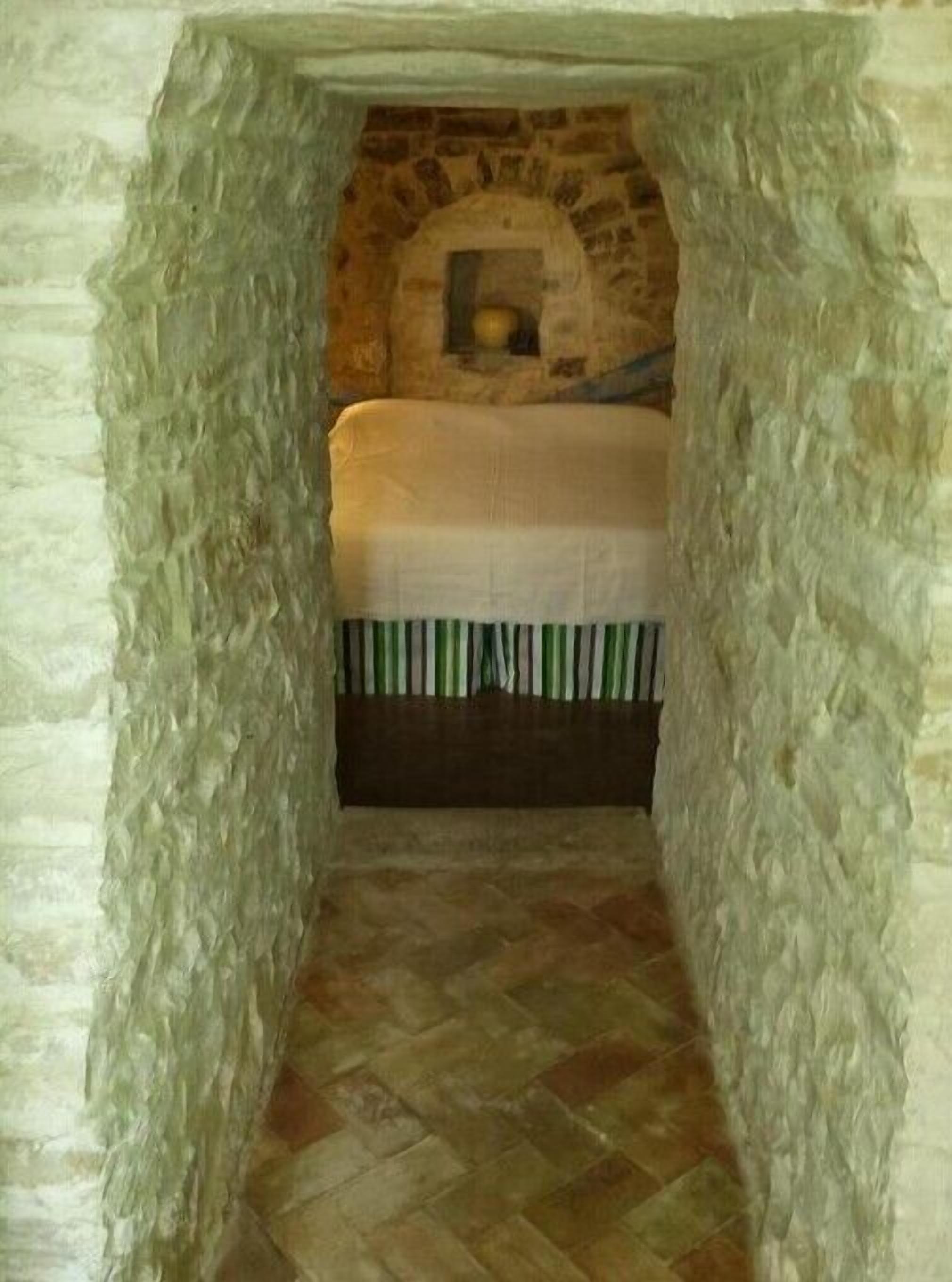 A narrow stone-walled room with a bed at the end.