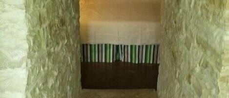 A narrow stone-walled room with a bed at the end.