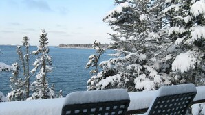Zona salotto esterna innevata con sedie e vista su un lago e alberi.