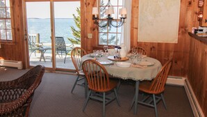 Un interno in legno con un tavolo da pranzo apparecchiato per sei persone, sedie, un lampadario e vista sul mare attraverso una porta in vetro.