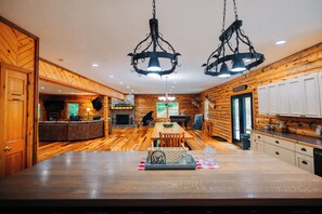 A log cabin interior with a dining area, kitchen, and a stone fireplace. - Secluded, Private 5000 Square Foot Luxury Lodge Located On 20 Wooded Acres. (Cambridge)