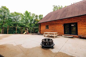 A wooden cabin with a patio, a swing set, and a fire pit. - Secluded, Private 5000 Square Foot Luxury Lodge Located On 20 Wooded Acres. (Cambridge)