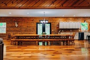 A wooden interior with a large dining table, benches, a chandelier, and a view through a window. - Secluded, Private 5000 Square Foot Luxury Lodge Located On 20 Wooded Acres. (Cambridge)