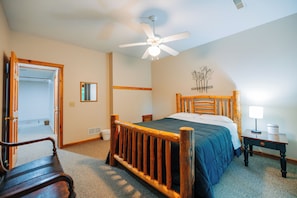 A bedroom with a wooden bed, a ceiling fan, a nightstand, and a lamp.