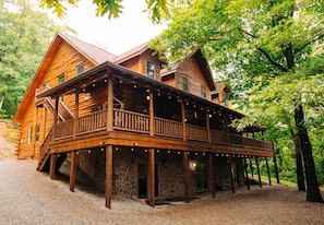 A log cabin with a stone foundation, a wooden deck, and a porch with string lights.