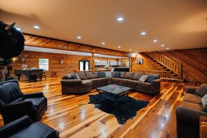 A spacious living area with a large L-shaped sectional sofa, a piano, and a dining table.
