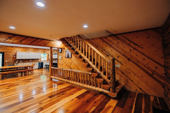 A wooden interior with a staircase, wooden floors, and a kitchen area. - Secluded, Private 5000 Square Foot Luxury Lodge Located On 20 Wooded Acres. (Cambridge)