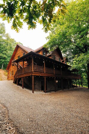 A wooden cabin with a deck and string lights, surrounded by trees.