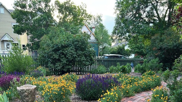 Un jardin agrémenté d’un chemin en briques, de différentes plantes à fleurs et d’un vase décoratif.