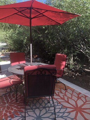 A patio area with a round table, red chairs, and a red umbrella.