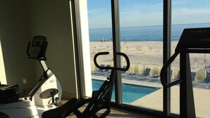 A gym with exercise equipment and a large window overlooking a beach and pool. - The Leeway,  Beautiful Gulf Front Condo on the Gulf of Mexico (Gulf Shores)