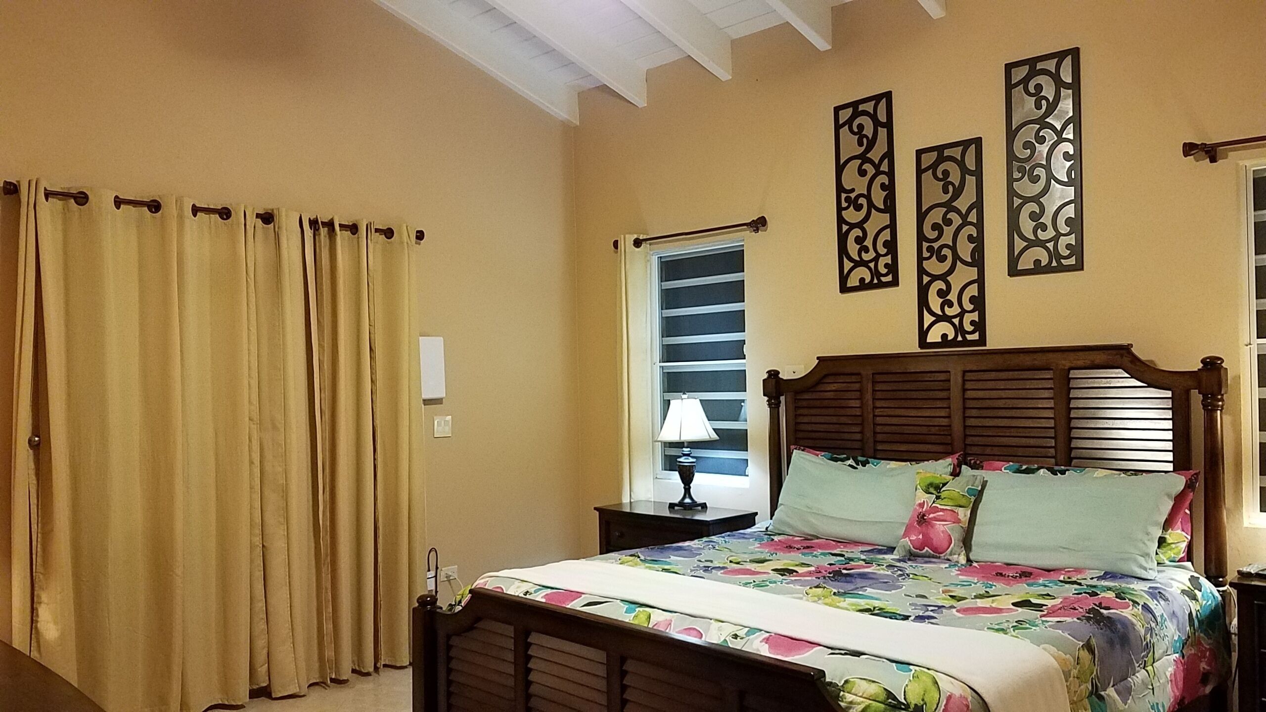 Une chambre à coucher avec un lit en bois, des rideaux beiges, une table de chevet avec une lampe et des œuvres d’art décoratives au mur.