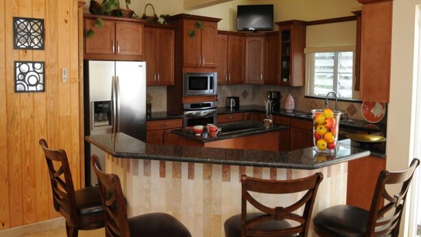A kitchen with wooden cabinets, a stainless steel refrigerator, a microwave, and a large island with chairs.