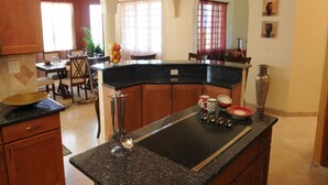A kitchen with a granite countertop, wooden cabinets, a black stovetop, and a dining area with a table and chairs.