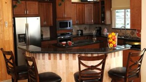 A kitchen with wooden cabinets, a refrigerator, microwave, and a large island with bar stools.