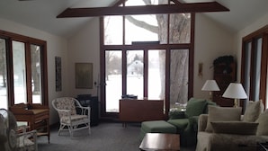 A cozy living room with a high ceiling, large windows, and a view of a snowy landscape. - Bay Beach house. No roads to cross to beach.  Private beach.  (Fort Erie)