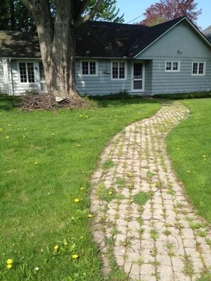 A paved pathway leading to a house with a large tree and a grassy lawn. - Bay Beach house. No roads to cross to beach.  Private beach.  (Fort Erie)