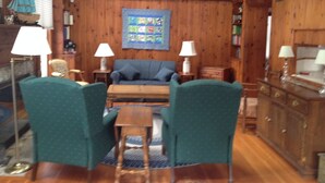 A cozy living room with a wooden ceiling, a blue sofa, two green armchairs, a wooden coffee table, and two side tables with lamps. - Bay Beach house. No roads to cross to beach.  Private beach.  (Fort Erie)