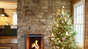 A cozy room with a stone fireplace, a Christmas tree, and wooden floors.