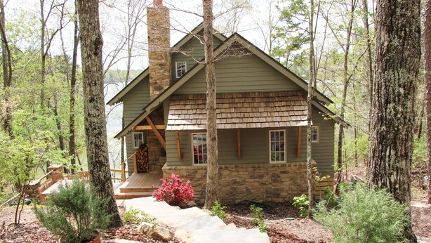 A rustic cabin with a stone chimney, wooden deck, and a stone foundation.
