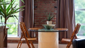 A round glass table with a green bowl and a potted plant, flanked by two bamboo chairs, in a room with brick walls and a window. - Very Special Downtown Asheville Loft  (Asheville)