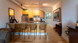 A modern kitchen with a central island, bar stools, wooden cabinets, and a refrigerator. - Very Special Downtown Asheville Loft  (Asheville)