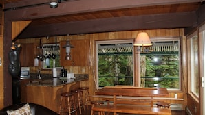 A wooden interior with a kitchen, dining area, and large windows. - CABIN LOOKING ACROSS THE SKY RIVER AT THE WILD SKY WILDERNESS (Skykomish)
