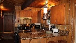 A kitchen with wooden cabinets, granite countertops, a stainless steel stove, a microwave, and a hanging light fixture. - CABIN LOOKING ACROSS THE SKY RIVER AT THE WILD SKY WILDERNESS (Skykomish)