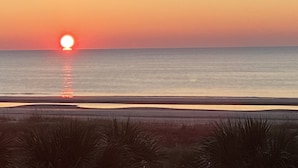 Un coucher de soleil sur une mer calme, avec une plage au premier plan.
