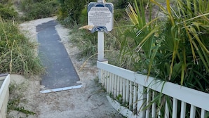 Une promenade en bois menant à une plage, avec un panneau d’information.