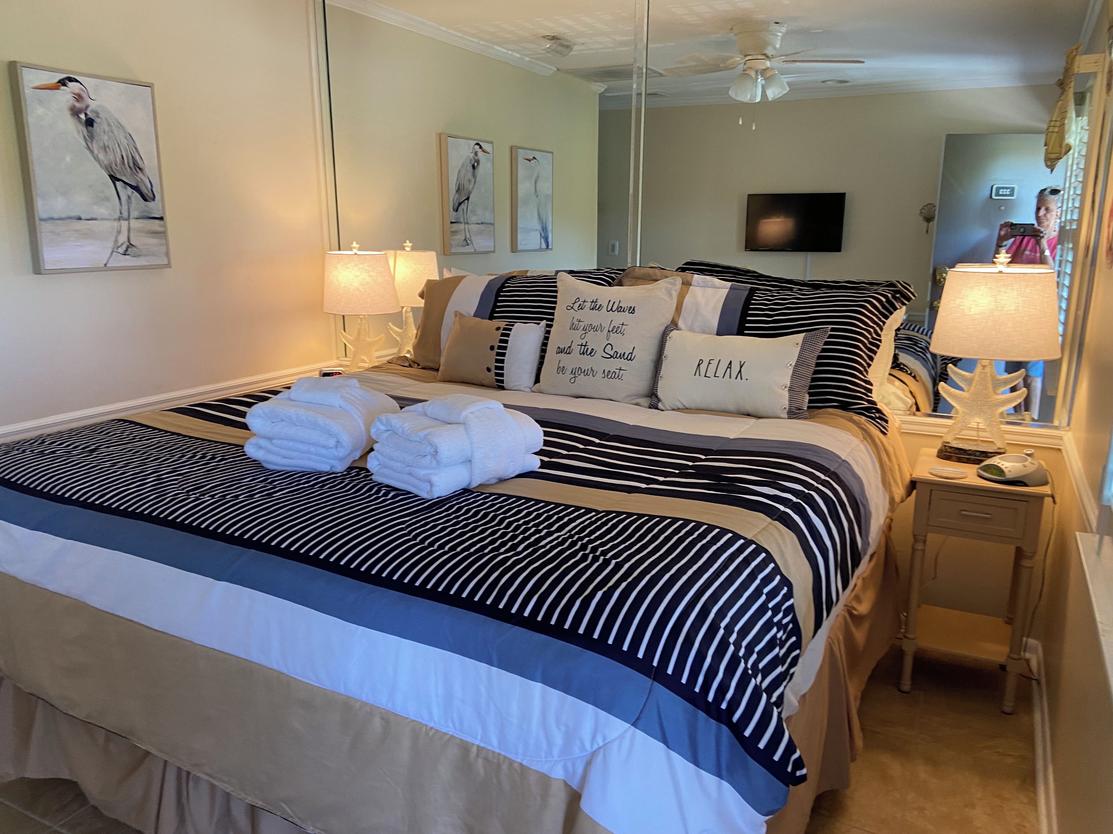 A neatly made bed with striped bedding and towels, a bedside lamp, and artwork on the wall.