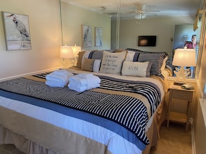 A neatly made bed with striped bedding and towels, a bedside lamp, and artwork on the wall. - Breakers Oceanfront Villa with Beautiful View of Ocean & Pool with a King Bed (Hilton Head Island)