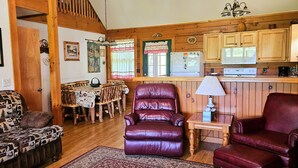 A cozy living room with a patterned sofa, a leather armchair, and a dining area with a table and chairs. - Deer Country Vacation Cabins #3 - Long Range View, Dogs Friendly (Waynesville)