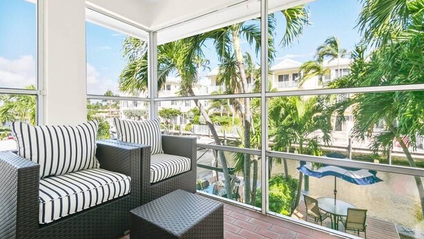 Ein Balkon mit Korbmöbeln und Blick auf Palmen sowie einen Pool.