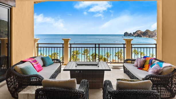 Ein Balkon mit Korbmöbeln, einer Feuerstelle und Blick auf das Meer und Palmen.