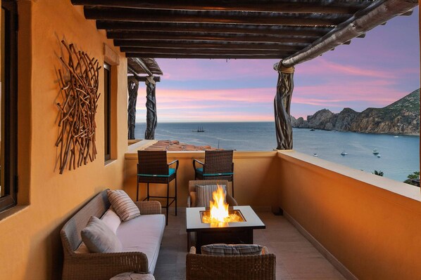 A balcony with a fire pit, wicker furniture, and a view of the sea and mountains.