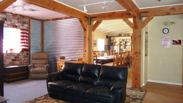 A living room with a black leather sofa, wooden beams, a brick wall, and a dining area with a table and chairs.