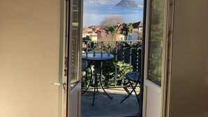 An open sliding door leading to a balcony with a table and chairs, overlooking a lake and mountains. - Hotel Loveno (Menaggio)