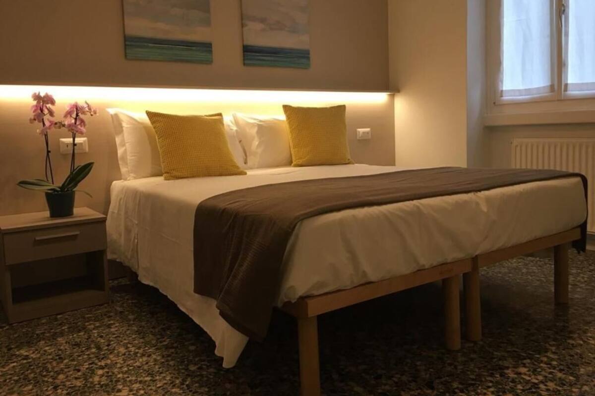 A hotel room with a bed, bedside table, lamp, and a window.