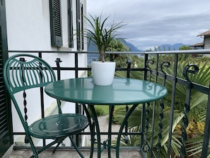 A small outdoor balcony with a round glass table, a chair, and a potted plant. - Hotel Loveno (Menaggio)