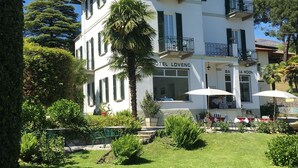 A two-story hotel with balconies, a garden with tables and chairs, and a sign reading "HOTEL LOVENO". - Hotel Loveno (Menaggio)