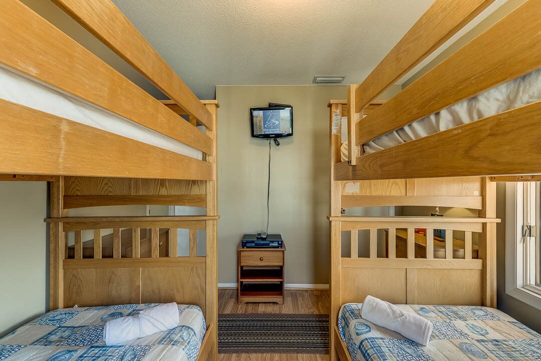 Une chambre avec un lit superposé, un téléviseur fixé au mur et une petite table de chevet en bois.