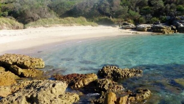 Una platja amb aigua turquesa cristal·lina, roques i un tram de sorra.